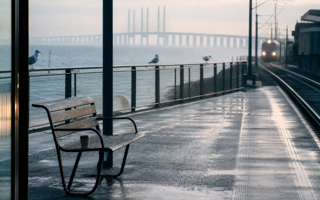 Tågplattform vid Öresund i gryningsljus, bron synlig i bakgrunden